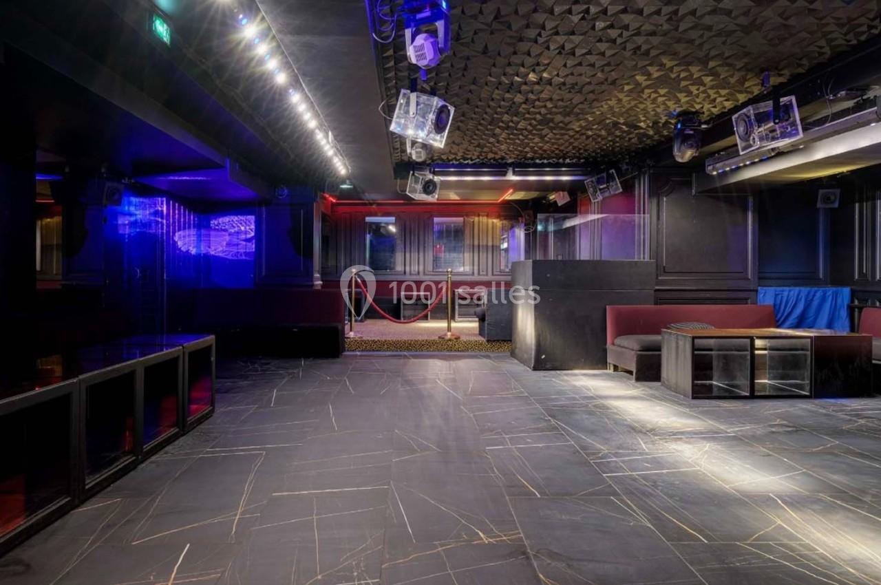 Salle de discothèque vide avec éclairage tamisé, piste de danse en marbre sombre et banquettes rouges.