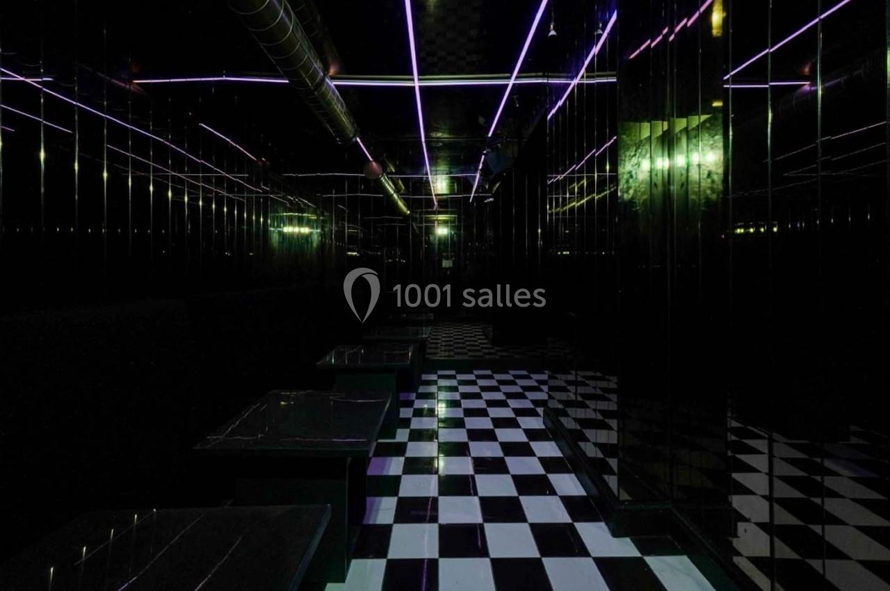 Salle sombre avec sol en damier noir et blanc, murs réfléchissants et éclairage néon violet au plafond.