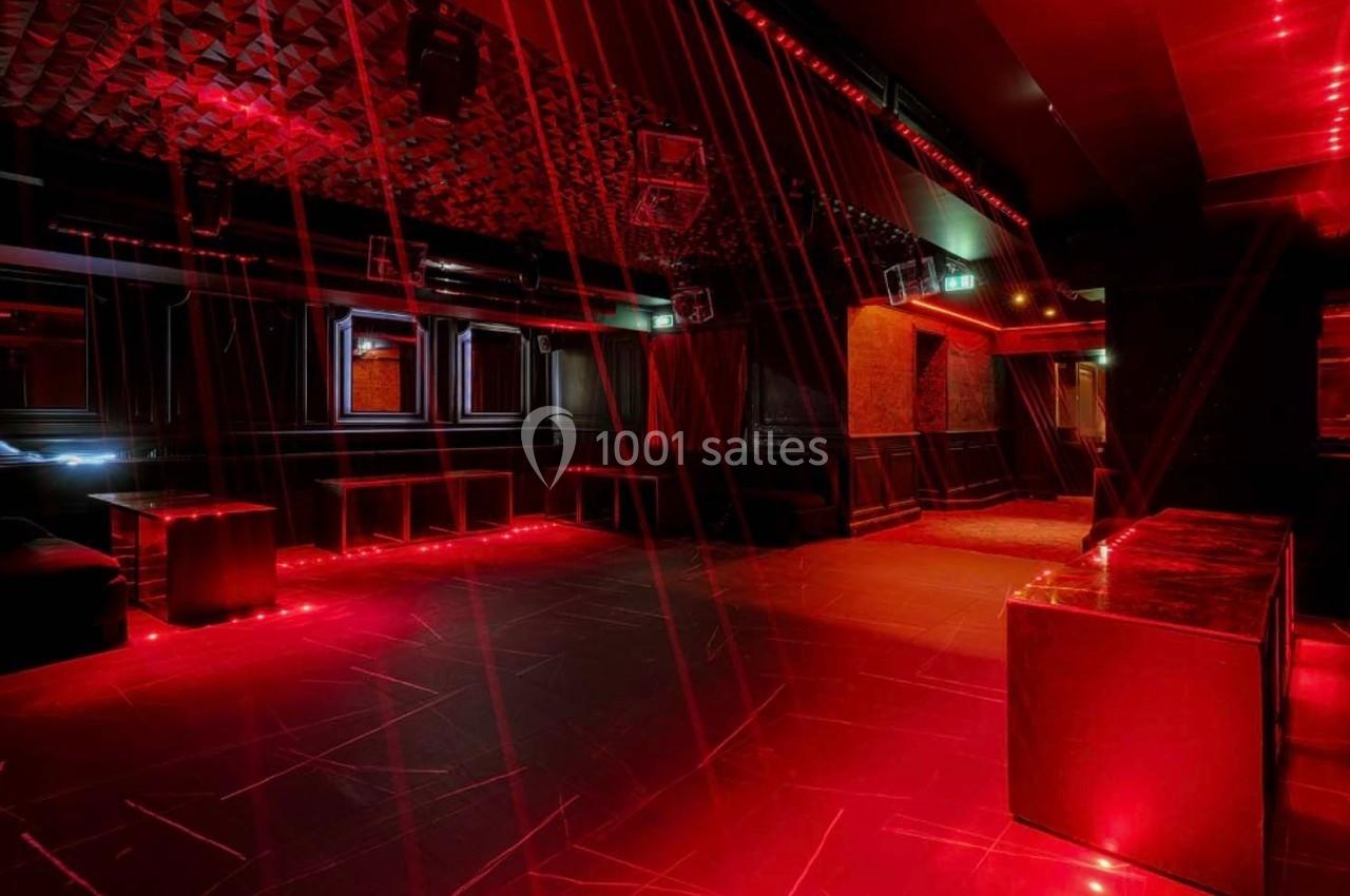 Salle de club vide avec éclairage rouge tamisé, murs sombres et plafond texturé.