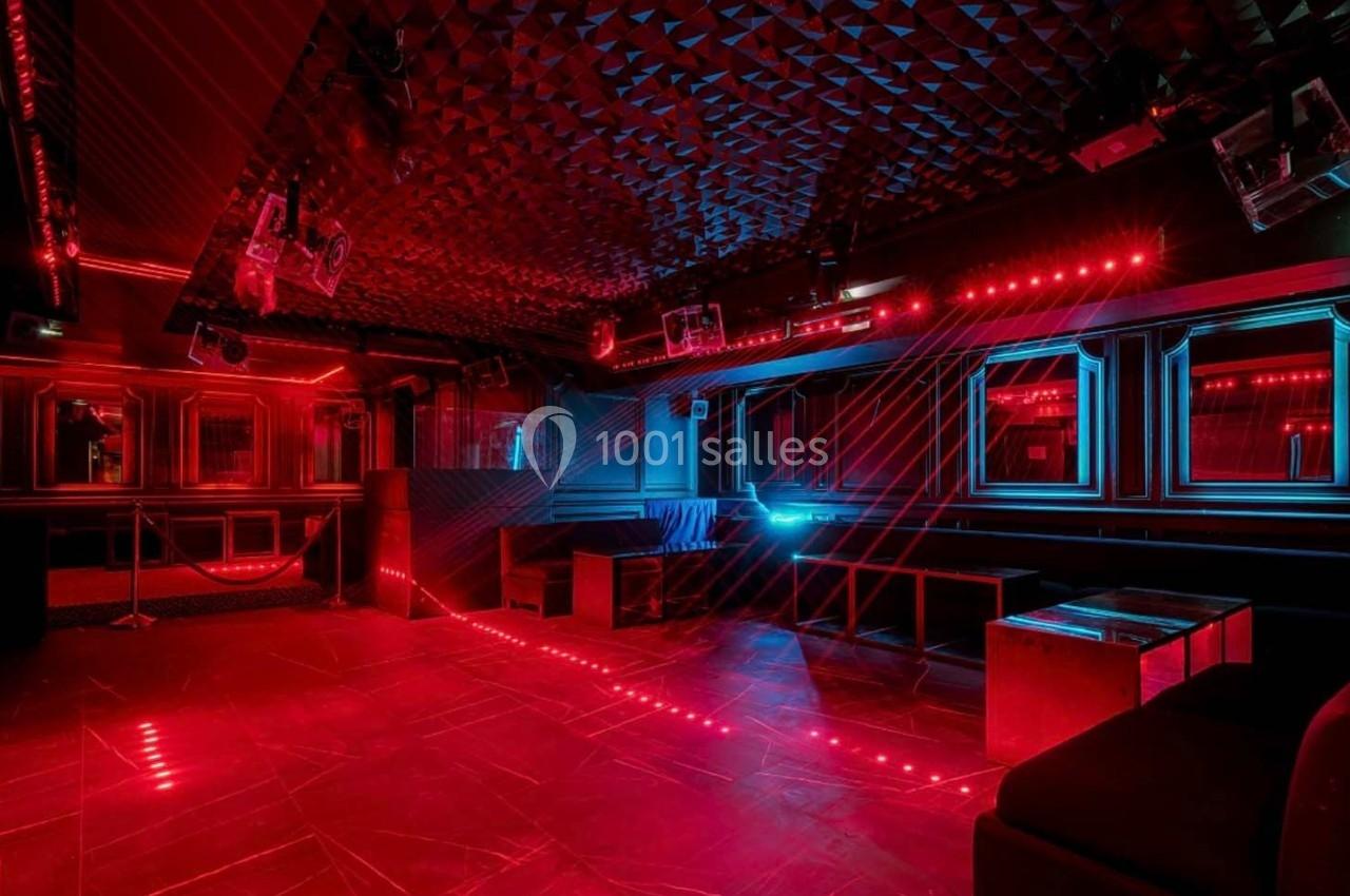 Salle de club vide avec éclairage rouge et bleu, murs capitonnés et mobilier minimaliste.