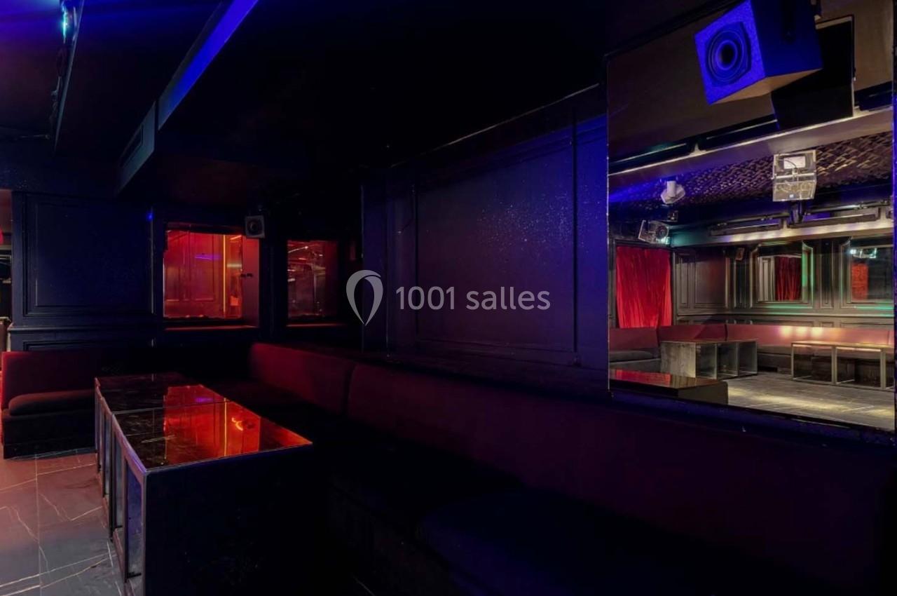 Salle sombre avec banquettes rouges, tables en marbre noir et éclairage tamisé aux tons rouges et bleus.