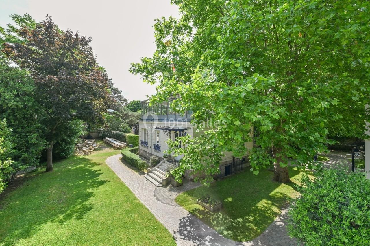 Maison entourée d'un jardin verdoyant avec des arbres et une allée pavée menant à l'entrée principale.