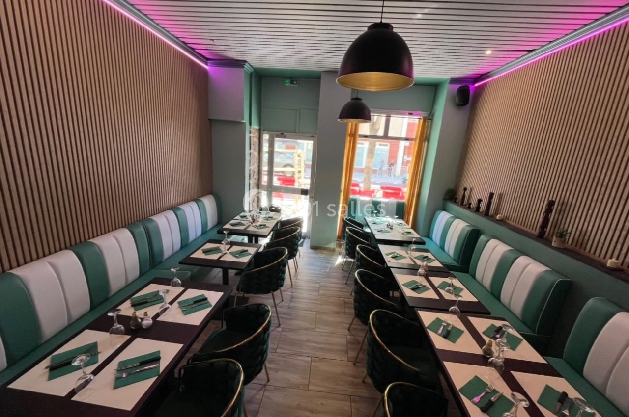 Salle de restaurant moderne avec tables dressées, banquettes vertes et éclairage tamisé.