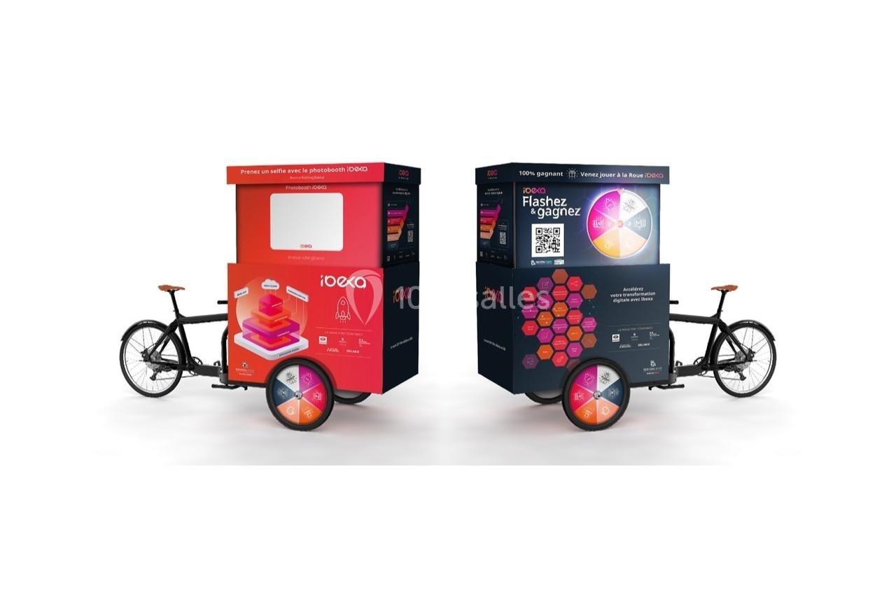 Deux vélos cargo avec des caissons publicitaires colorés, incluant un QR code et des visuels promotionnels.
