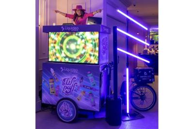 Deux personnes discutent gestuellement lors d'une soirée avec une DJ en arrière-plan et des lumières colorées.