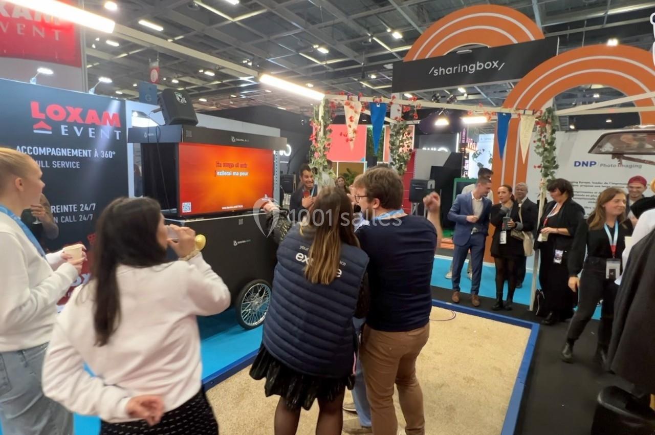 Des personnes interagissent et discutent dans un stand animé lors d'un événement professionnel en intérieur.