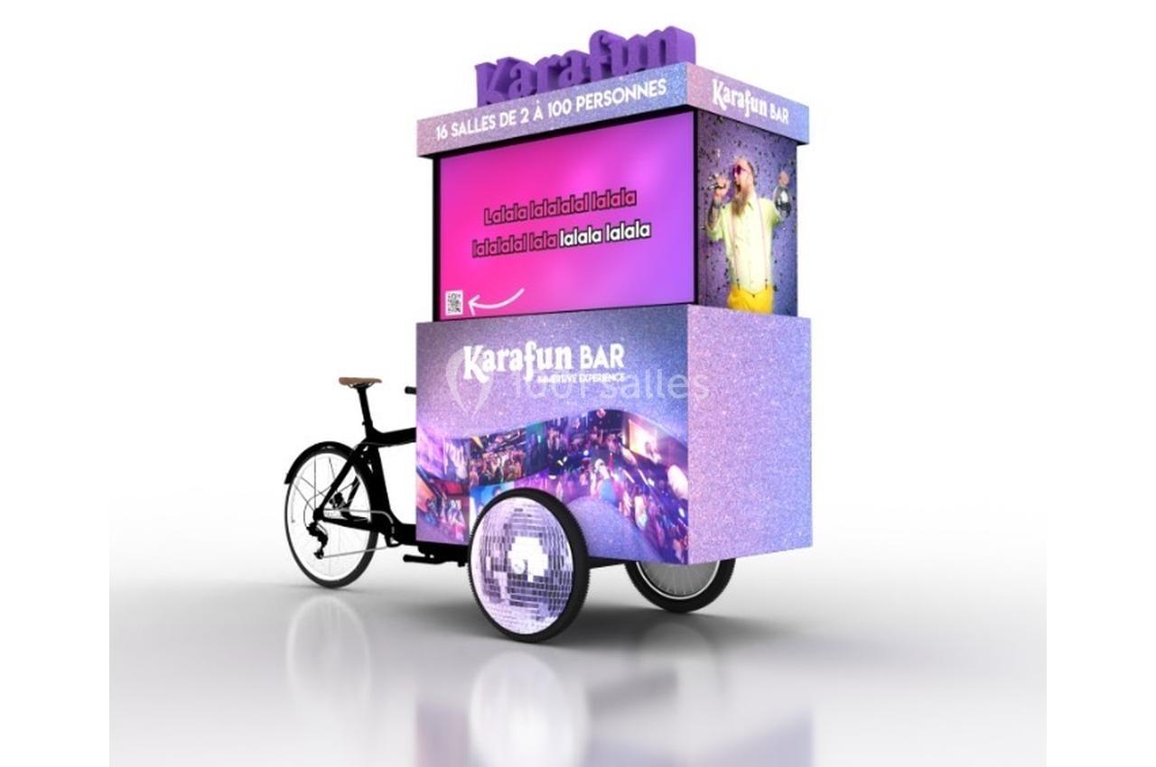 Triporteur promotionnel violet avec écran affichant des informations sur un bar karaoké et des images festives.