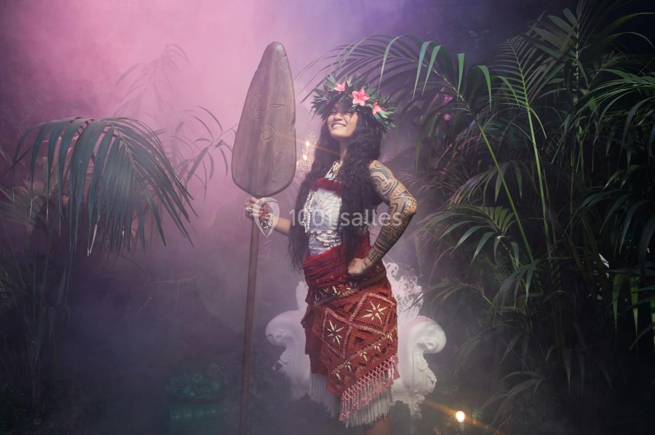 Femme en tenue traditionnelle polynésienne tenant une pagaie, entourée de végétation tropicale et de brume.