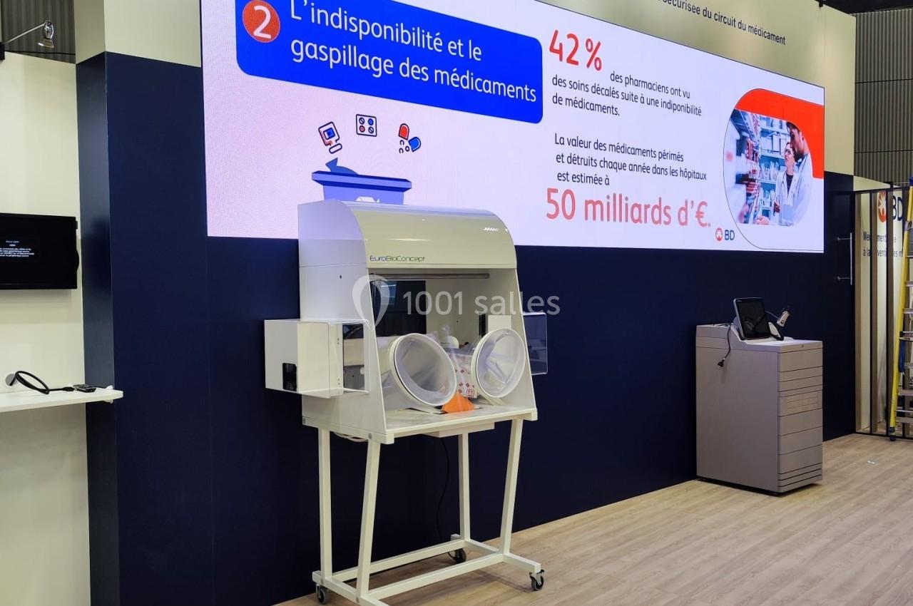 Stand d'exposition avec un écran affichant des données sur la gestion des médicaments et un équipement médical en avant-plan.