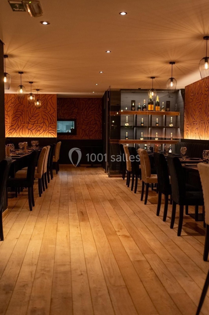 Salle de restaurant chaleureuse avec parquet en bois clair, murs décorés et étagères contenant des bouteilles.