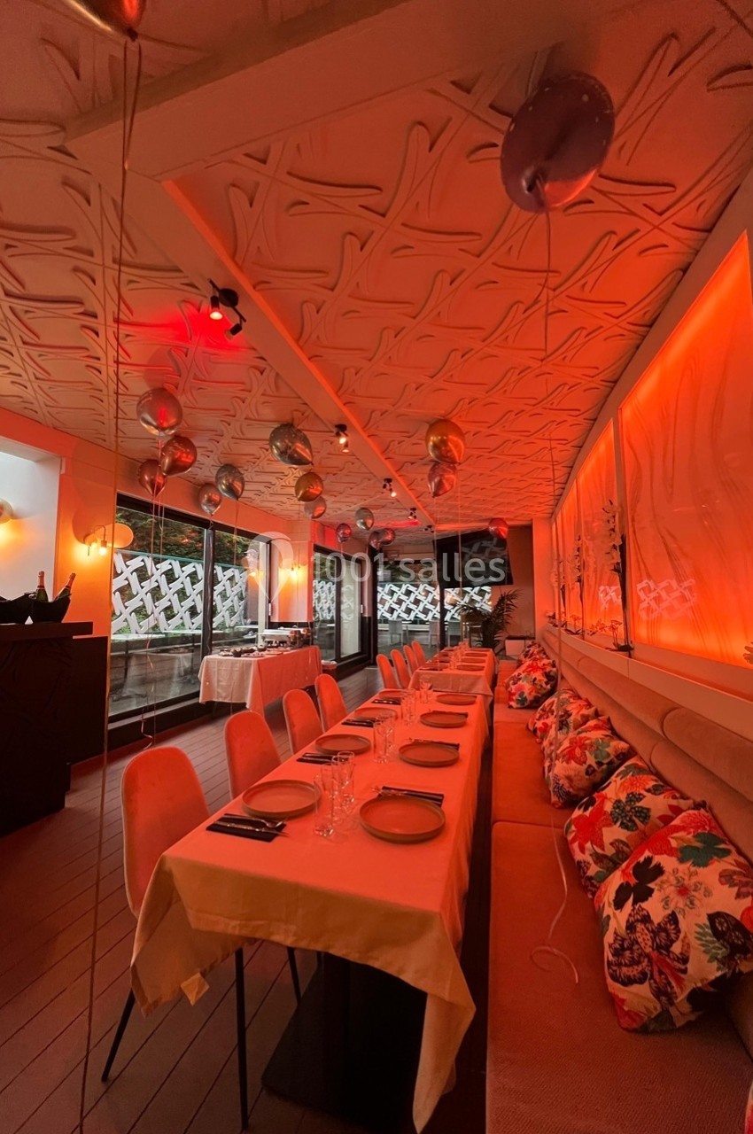 Salle de restaurant chaleureuse avec tables dressées, éclairage orange et décorations suspendues au plafond.