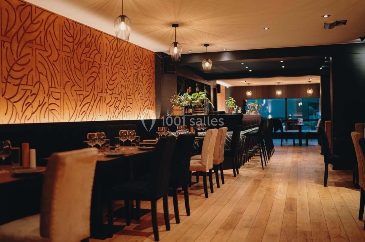 Salle de restaurant élégante avec tables dressées, chaises variées, éclairage tamisé et mur décoratif en bois sculpté.