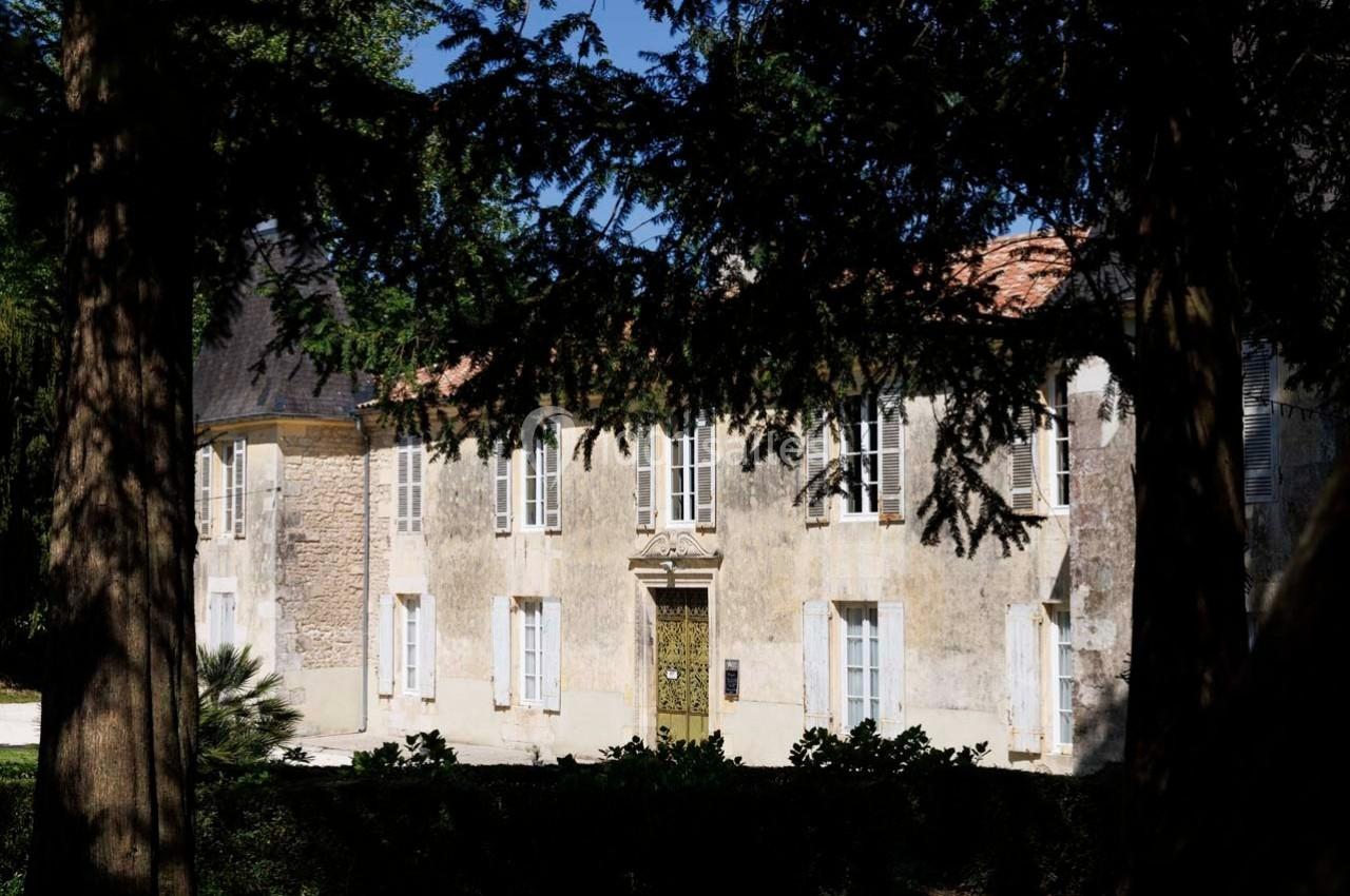 Façade d'un bâtiment ancien en pierre, entouré d'arbres et baigné de lumière naturelle.