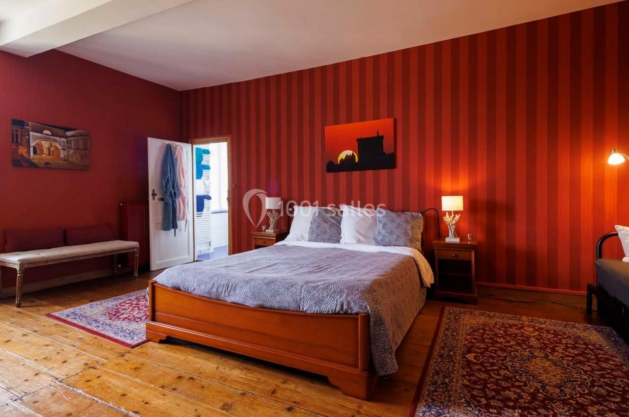 Chambre avec lit double, murs rouges à rayures, parquet en bois, tapis et éclairage doux.