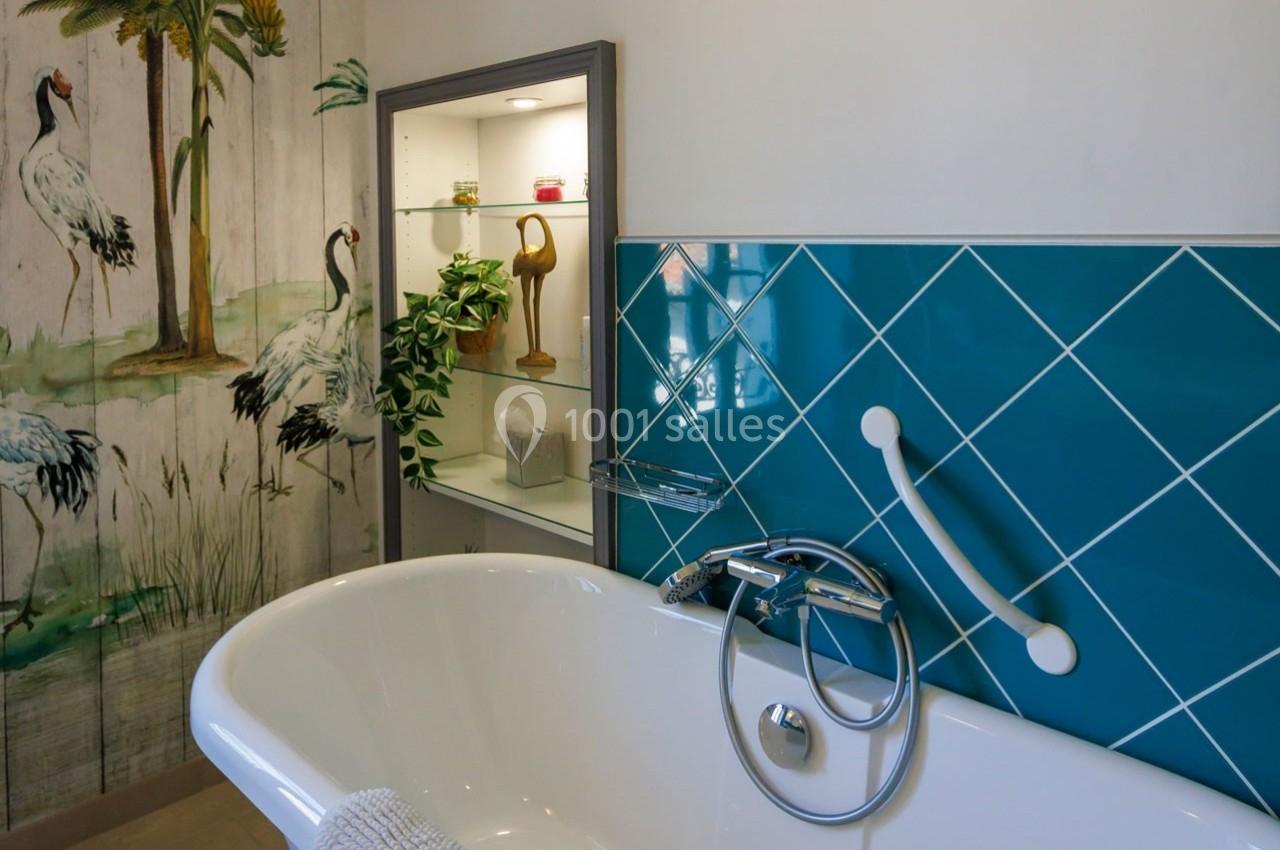 Baignoire blanche avec robinetterie moderne, carrelage bleu et fresque murale représentant des oiseaux et des plantes.