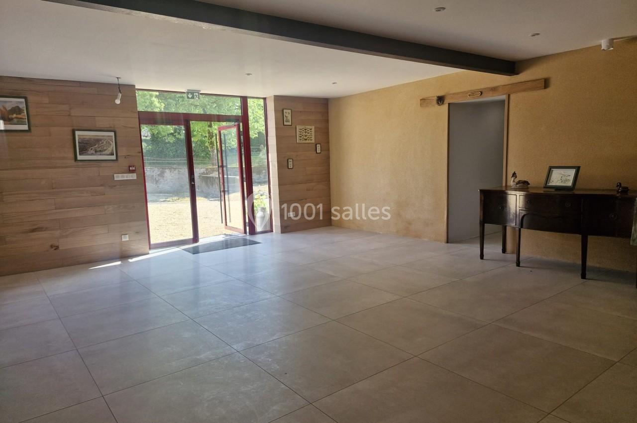 Salle lumineuse avec sol en carrelage clair, murs en bois et en crépi, ouverte sur un extérieur verdoyant.