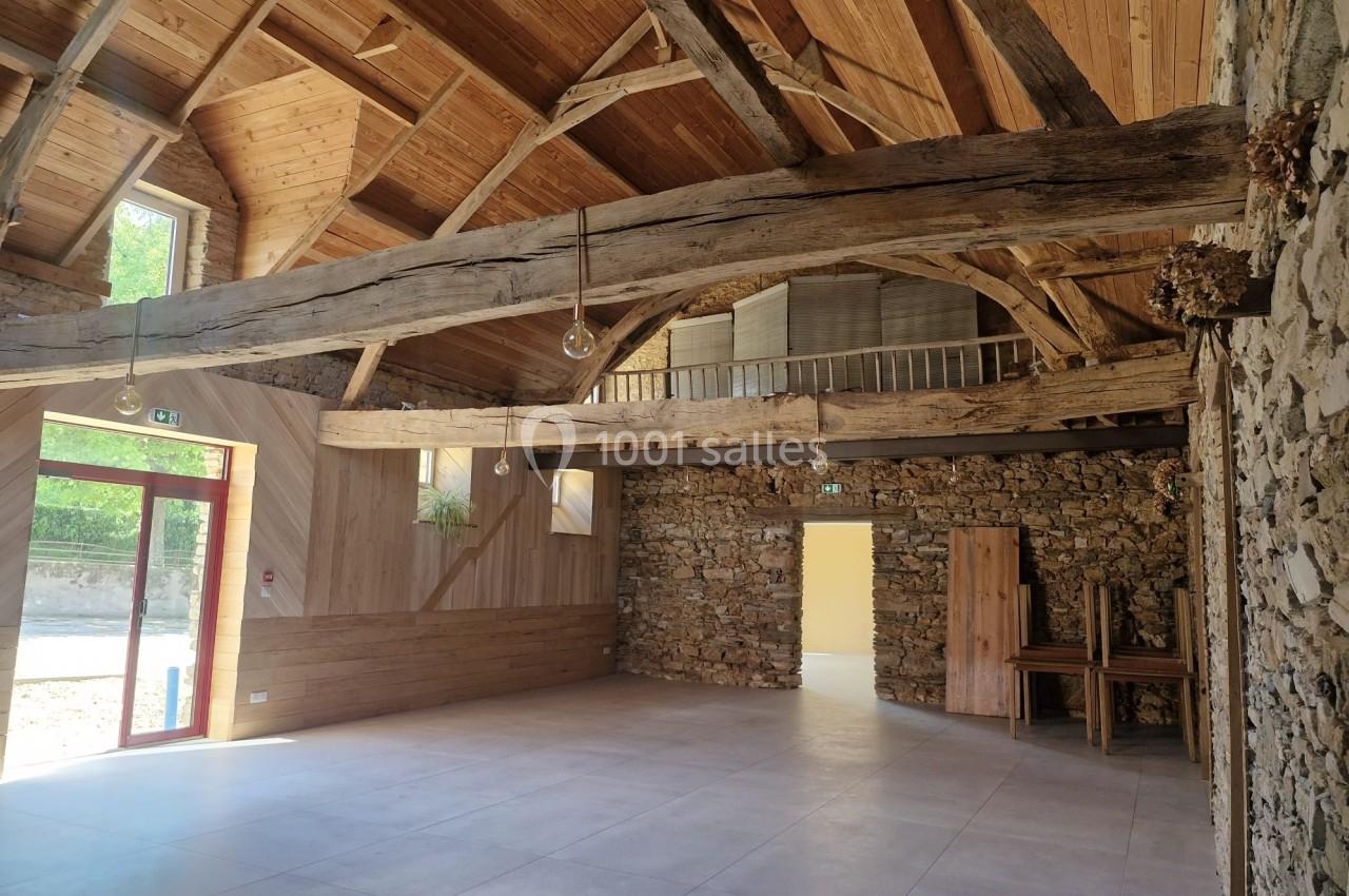 Salle intérieure rénovée avec poutres en bois apparentes, murs en pierre et grandes ouvertures lumineuses.