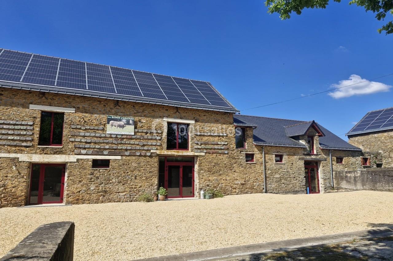 Bâtiments en pierre rénovés avec des panneaux solaires sur les toits, entourés d'une cour en gravier sous un ciel bleu.