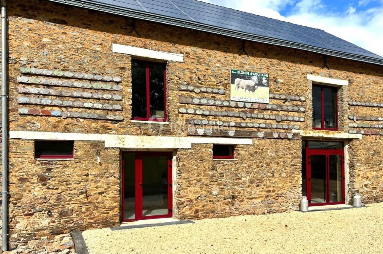 Façade en pierre d'un bâtiment avec fenêtres rouges, panneaux solaires sur le toit et une affiche agricole.