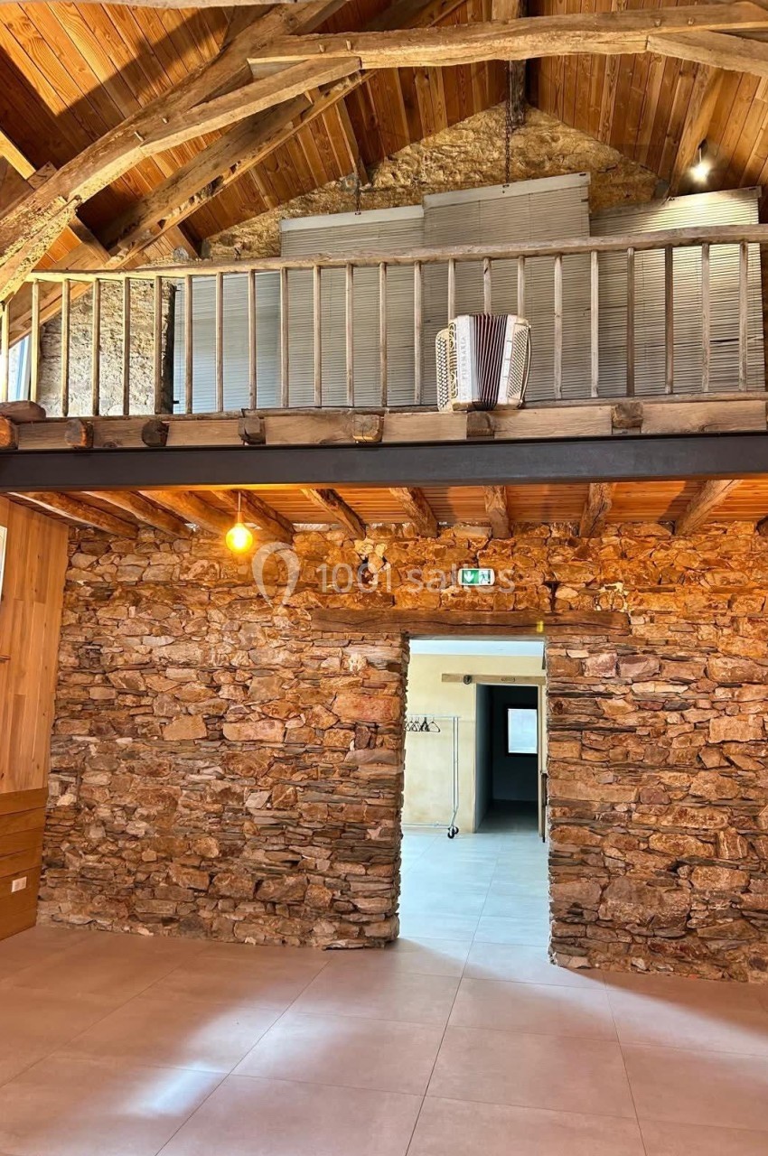 Intérieur d'une pièce en pierre avec un plafond en bois, une mezzanine et un accordéon posé sur la rambarde.