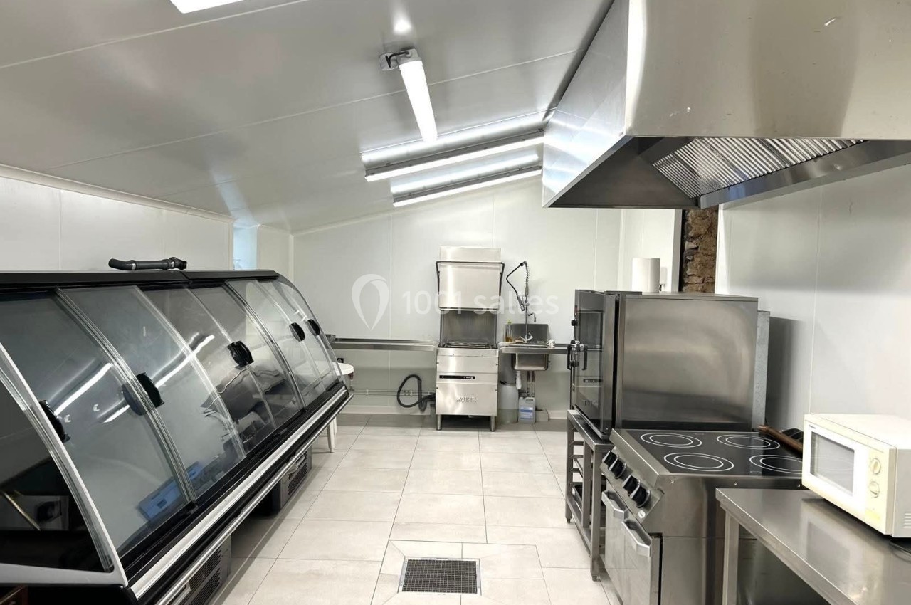 Cuisine professionnelle équipée avec réfrigérateur vitré, plaques de cuisson, hotte, four et micro-ondes.