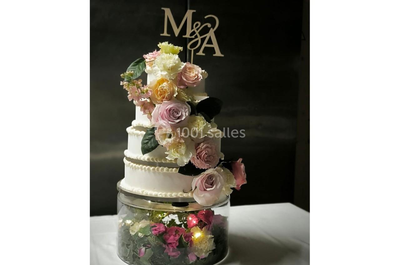 Gâteau de mariage à trois étages décoré de fleurs fraîches et posé sur une base transparente illuminée.
