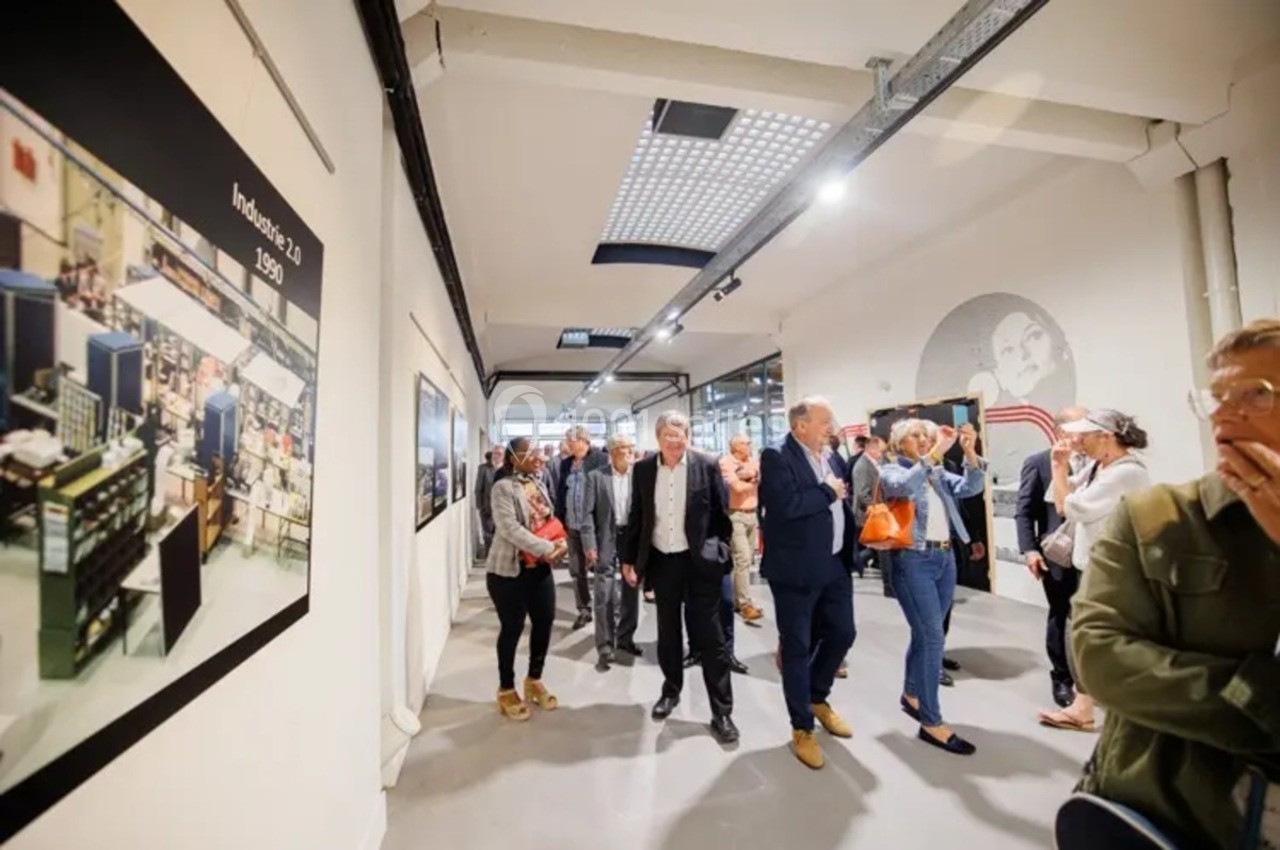 Un groupe de personnes visite une exposition dans une galerie moderne avec des photos accrochées aux murs.