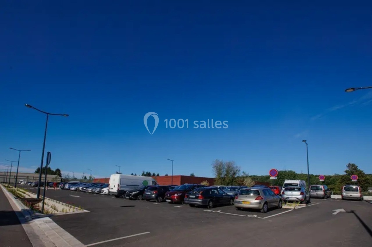 Parking extérieur avec plusieurs voitures garées, éclairé par des lampadaires sous un ciel bleu dégagé.