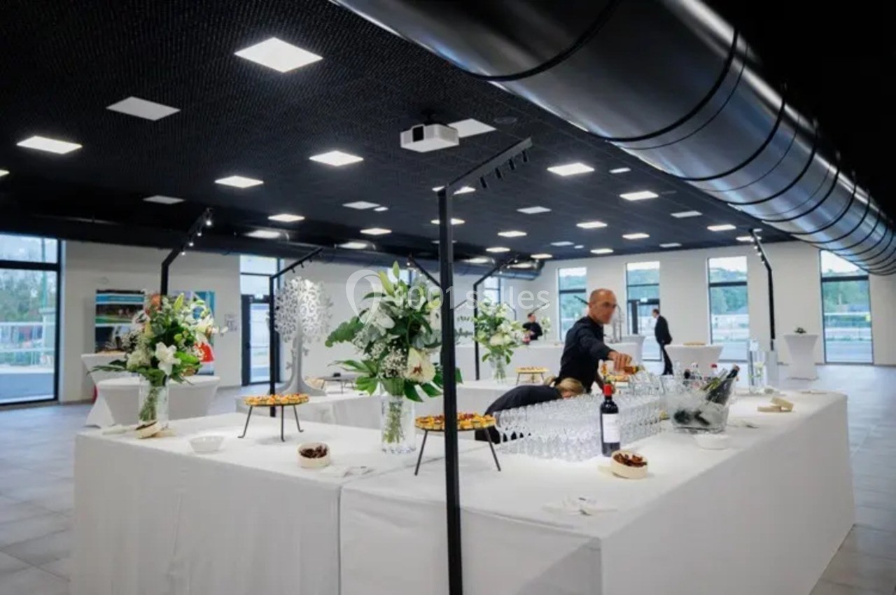 Table dressée pour un buffet avec fleurs, verres, bouteilles de vin et un serveur en arrière-plan dans une salle lumineuse.