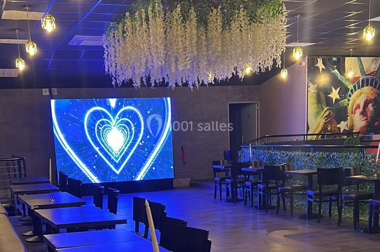Salle moderne avec tables, écran affichant un cœur lumineux et plafond décoré de plantes suspendues.
