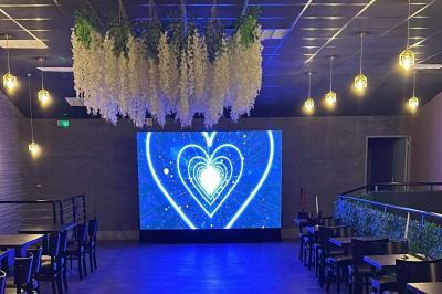 Miniature Location salle Saint-Soupplets (Seine-et-Marne) - The Taj #8 Salle moderne avec écran affichant des cœurs lumineux, tables et chaises noires, plafond décoré de fleurs suspendues.