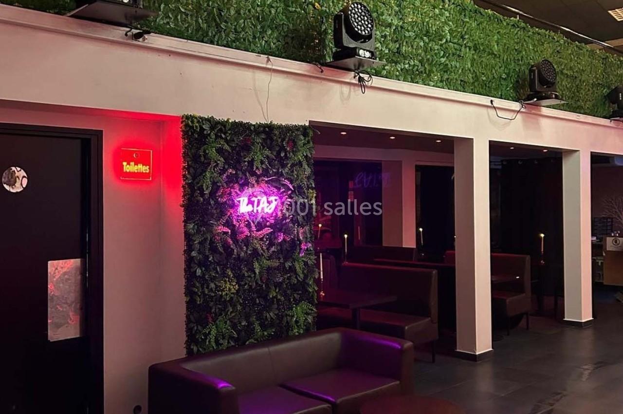 Mur végétal avec enseigne lumineuse rose ’LITAS’, banquettes et éclairage tamisé dans un espace intérieur moderne.