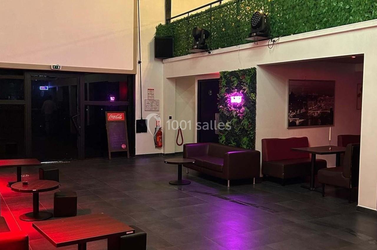 Salle moderne avec tables, banquettes, murs végétalisés et éclairage tamisé, donnant sur une entrée vitrée.