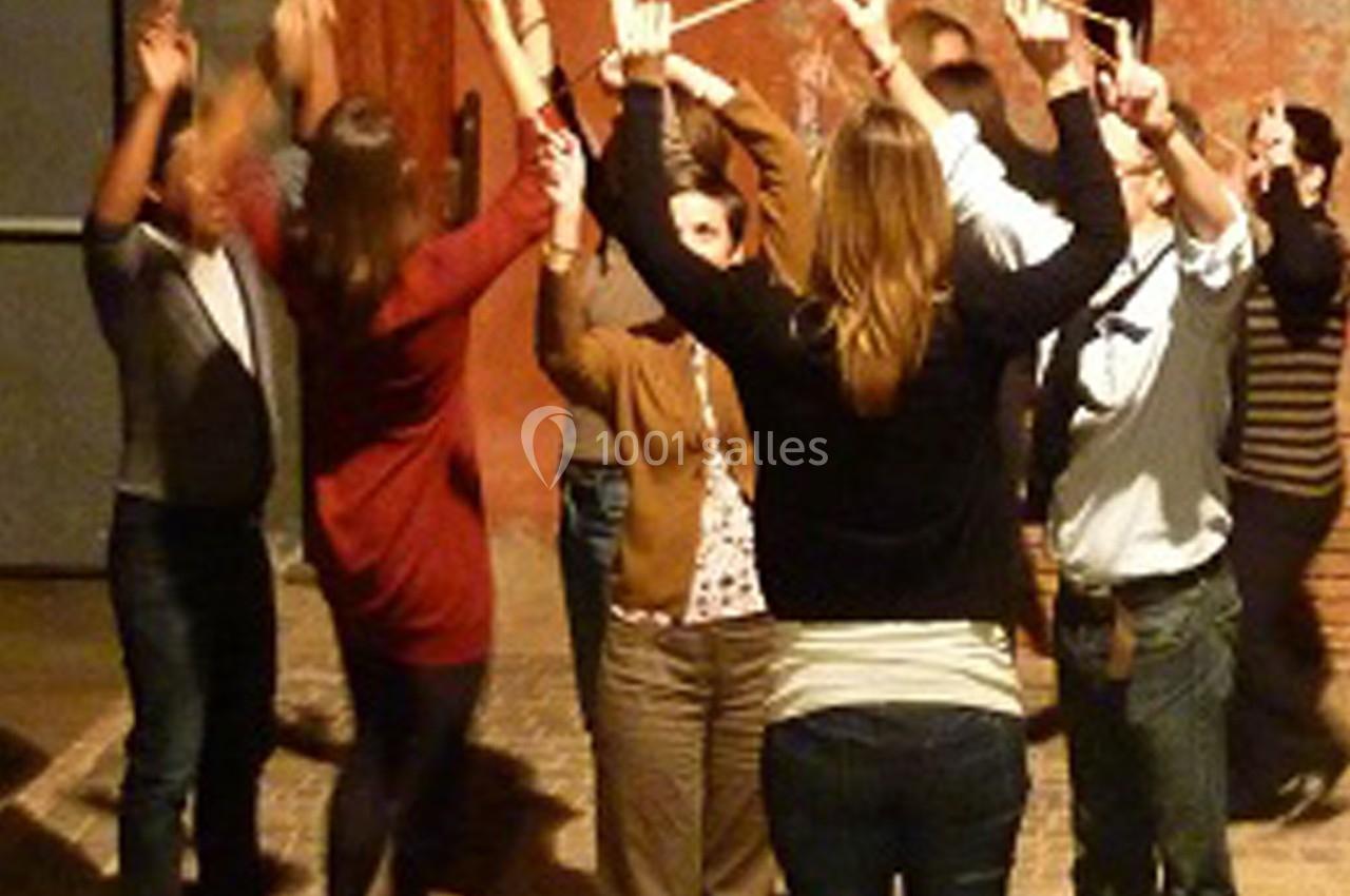 Des personnes debout en cercle, levant les bras et tenant des bâtons dans un espace intérieur faiblement éclairé.