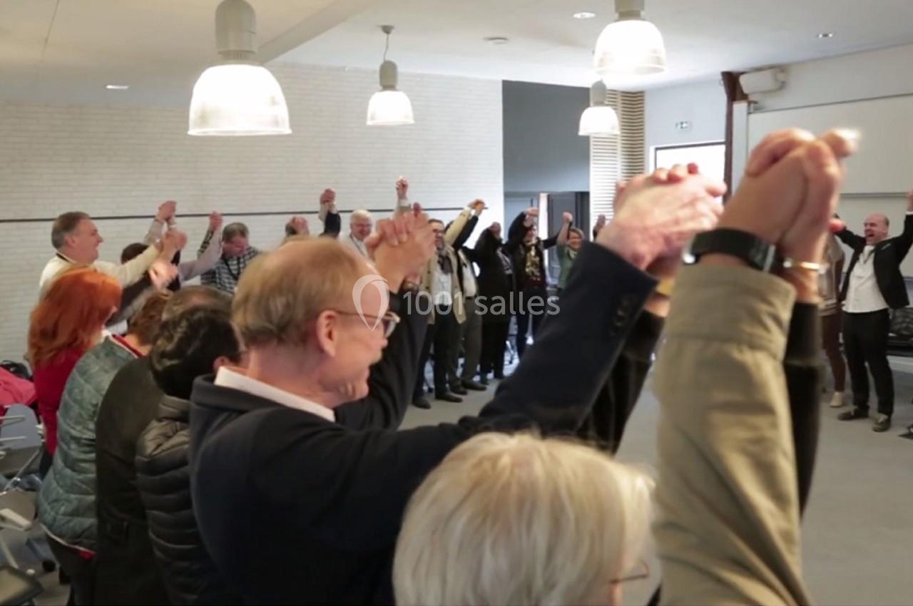 Des personnes debout en cercle dans une salle, levant les bras en l'air et se tenant par les mains.