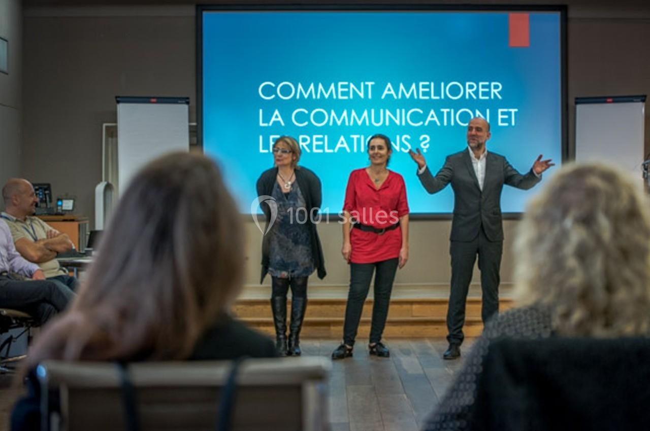 Trois personnes debout devant un écran de présentation affichant ’Comment améliorer la communication et les relations ?’.