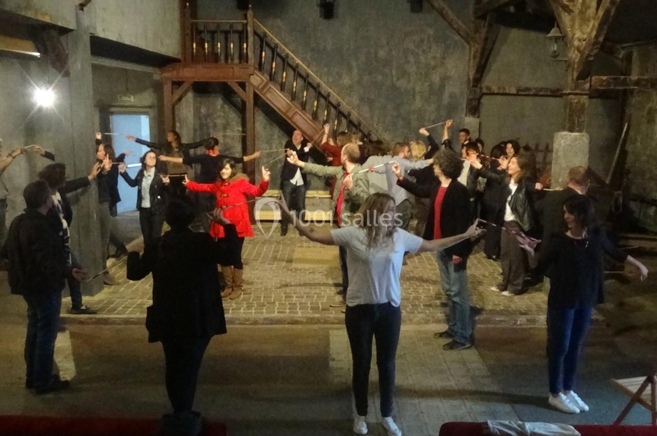 Un groupe de personnes participe à une activité collective dans une grande salle au décor rustique.