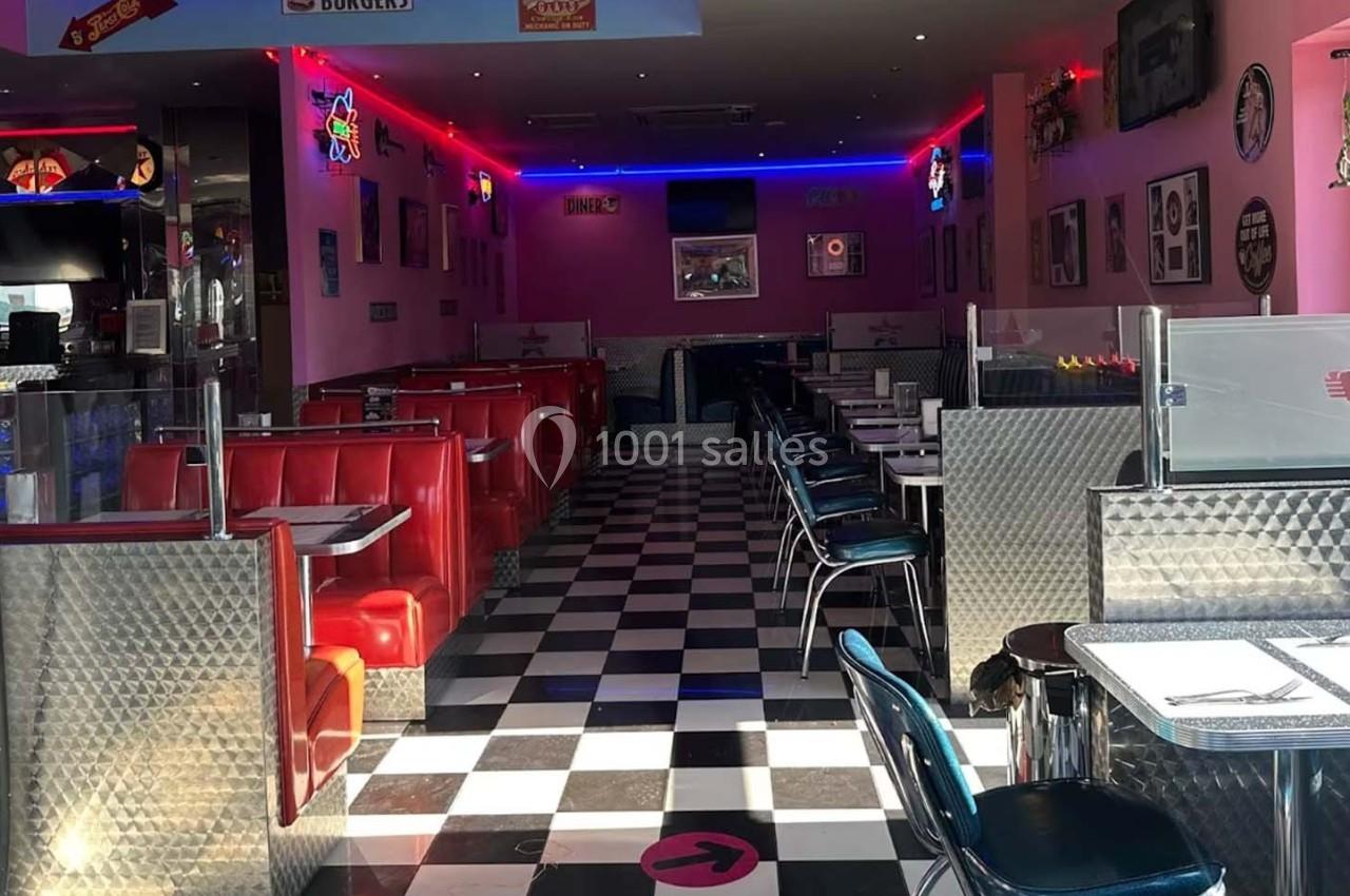 Salle de restaurant au style rétro américain avec banquettes rouges, sol en damier et décoration vintage.