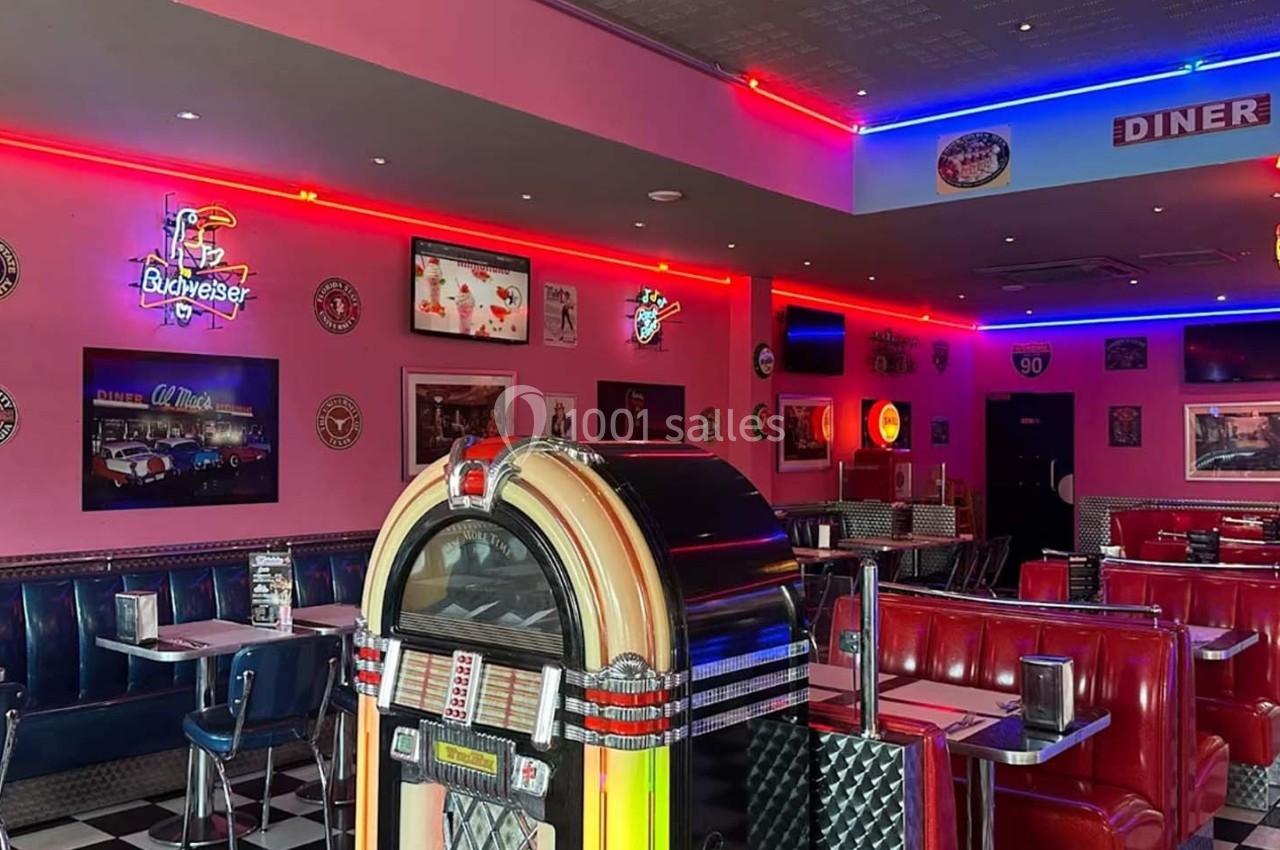 Intérieur d'un diner rétro avec jukebox, banquettes rouges, décorations murales et éclairage néon coloré.