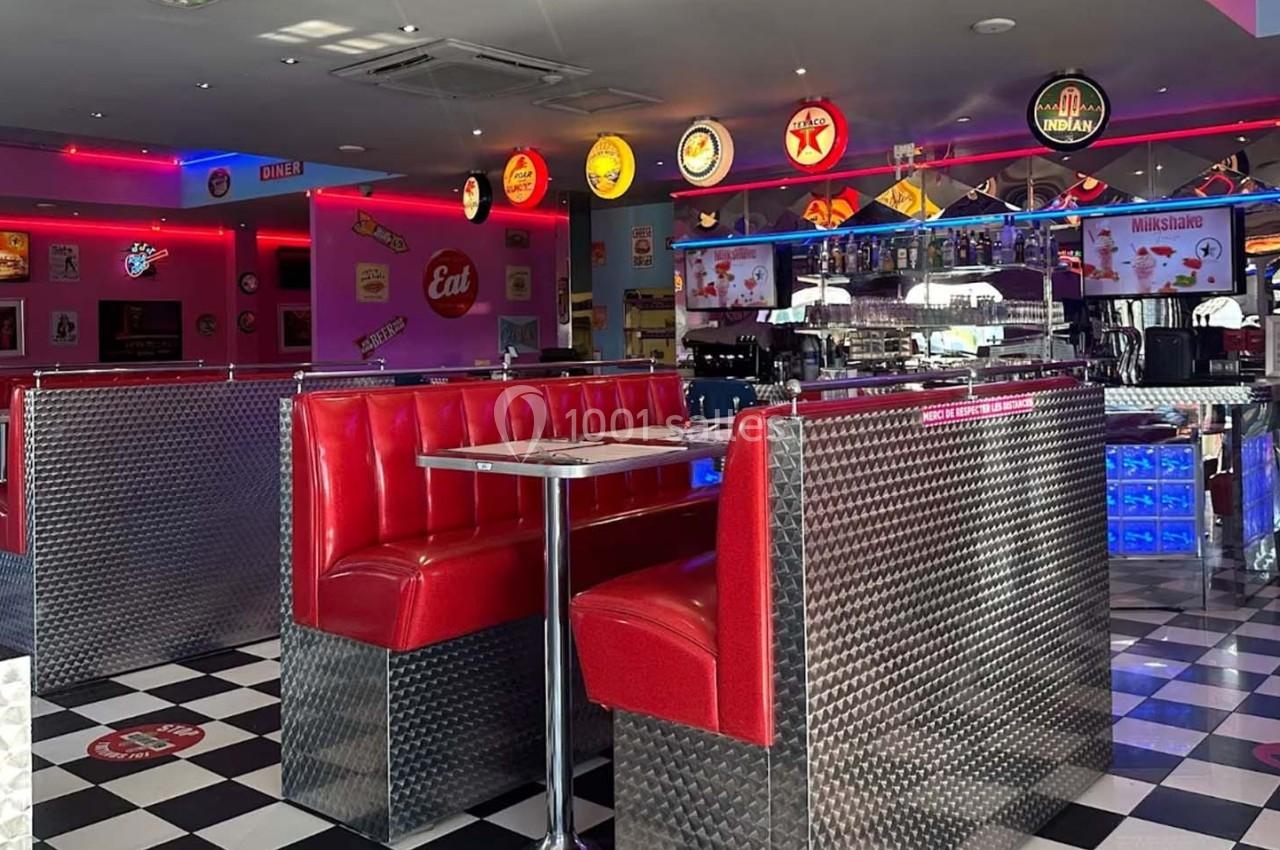 Intérieur d'un diner rétro avec banquettes rouges, sol en damier noir et blanc, et décorations vintage colorées.