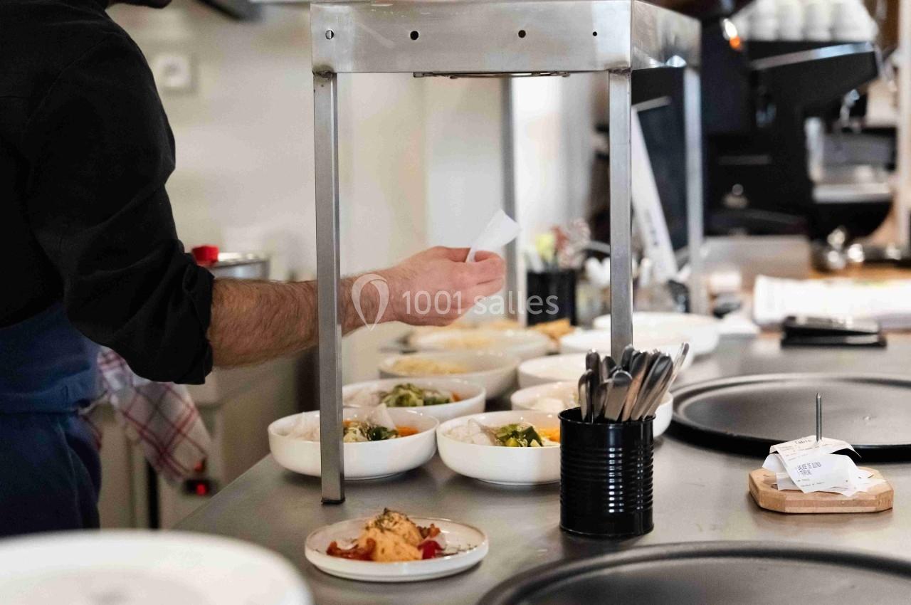 Un cuisinier prépare des plats dans une cuisine professionnelle, avec des bols alignés sur le plan de travail.