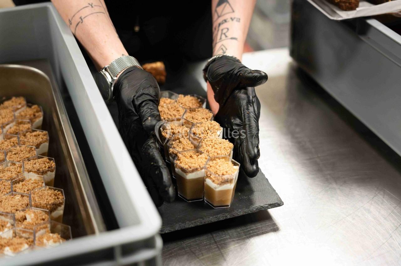 Une personne portant des gants noirs dispose des verrines garnies de crumble sur un plateau noir.
