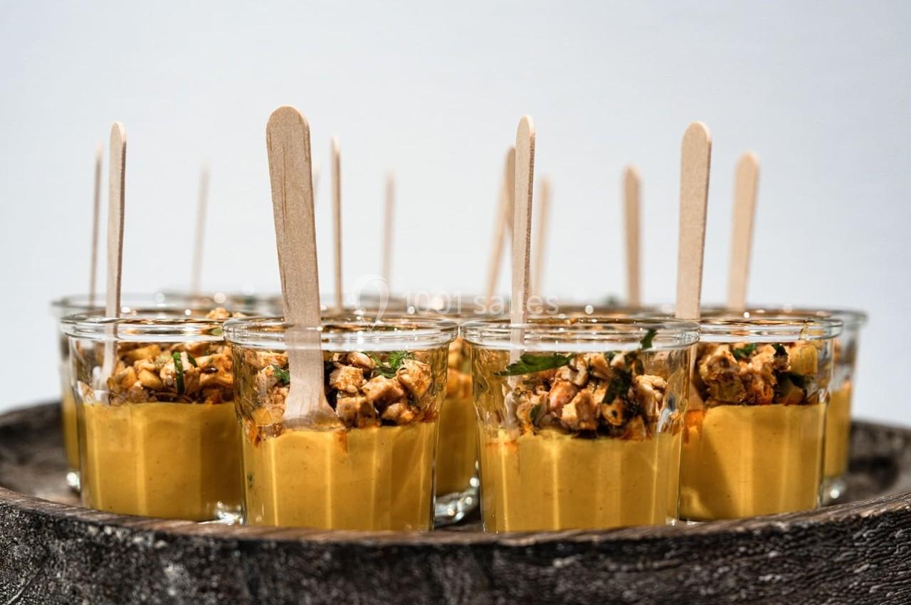 Verrines de soupe jaune garnies de morceaux croustillants et présentées avec des bâtonnets en bois.