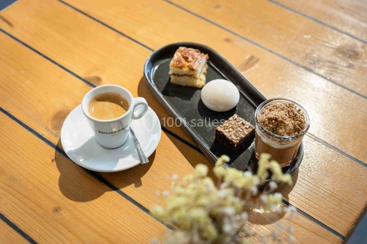 Tasse de café avec un plateau de desserts variés sur une table en bois clair.