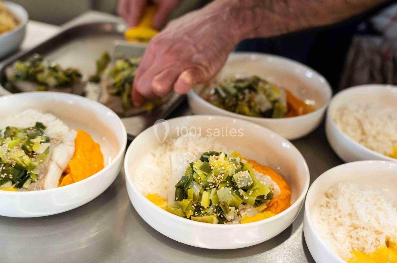 Une main sert un plat composé de poisson, purée orange, riz et légumes verts dans des bols blancs.