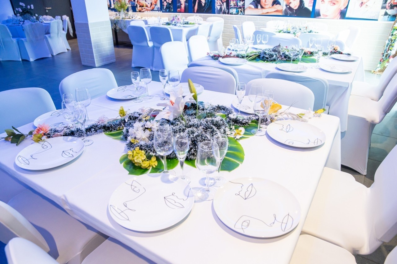 Table décorée pour un événement avec nappes blanches, vaisselle élégante, verres et centre de table floral.
