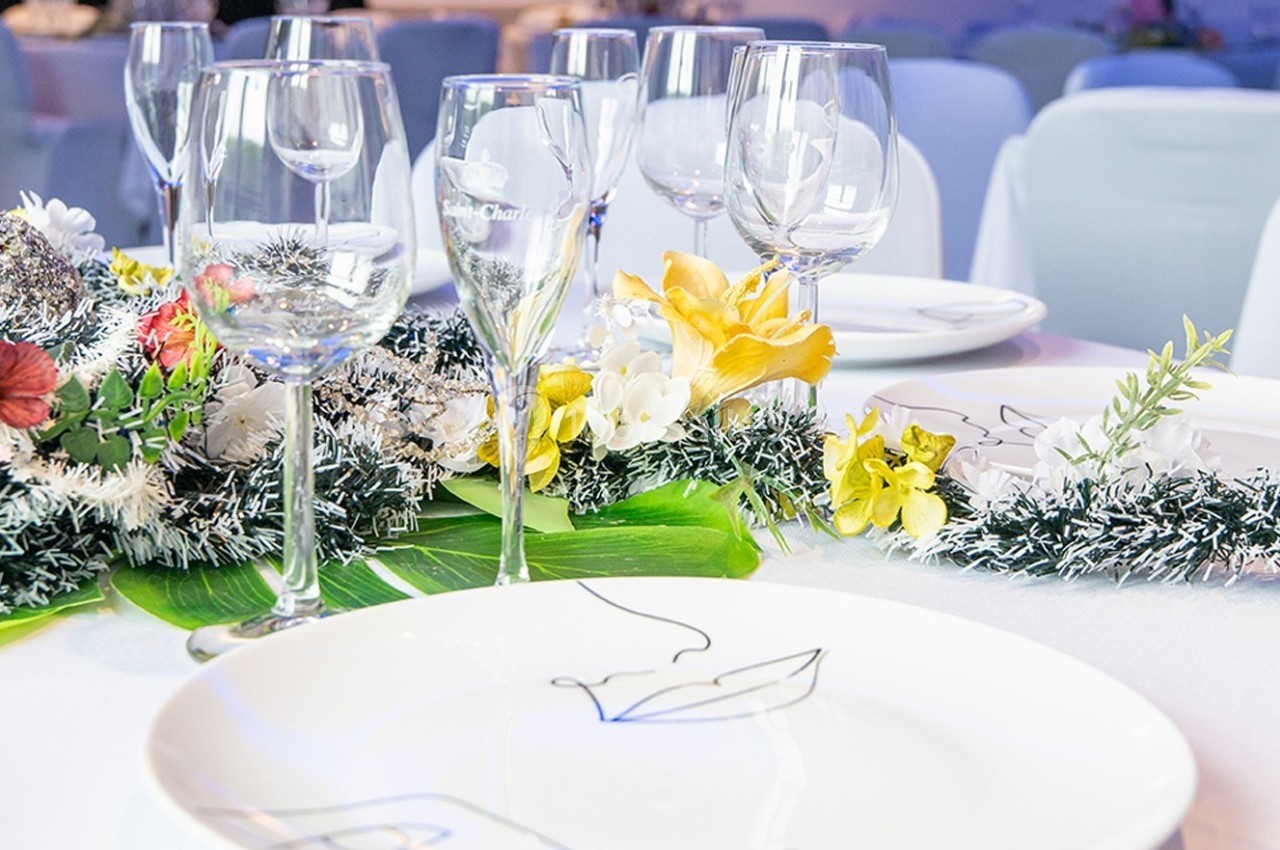 Table élégamment dressée avec assiettes blanches, verres en cristal et décoration florale colorée.