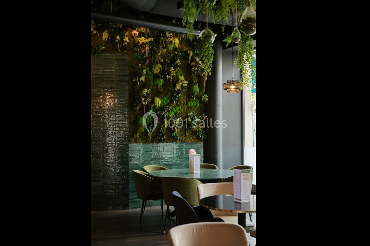 Mur végétal décoratif dans un intérieur moderne avec des tables, des chaises et une suspension lumineuse.