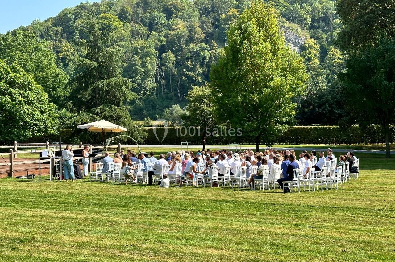 Cérémonie en plein air avec des invités assis en cercle sur des chaises blanches, entourés de verdure et d'arbres.