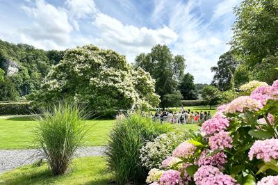Miniature Location salle Namur (Namur) - Château de Beez #17 Groupe de personnes assises en extérieur lors d'une cérémonie, entourées d'arbres et de fleurs sous un ciel partiellement…